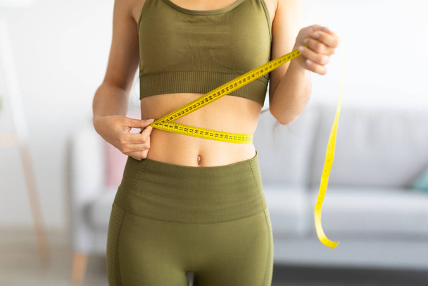 Cropped view of slim Indian woman measuring her waist with tape measure at home, closeup - Photo, Image