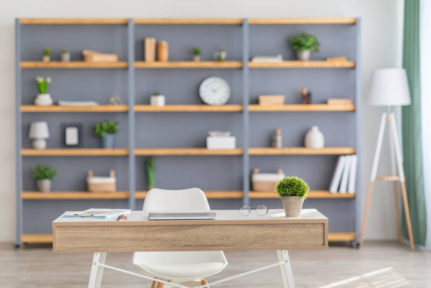 Home Office Interieur. Tisch mit Laptop, Regale mit Topfpflanzen, Dekorelemente und Accessoires, graue Wand - Foto, Bild