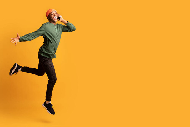 Смішний емоційний чорний хлопець стрибає в повітрі і розмовляє на мобільному телефоні
 - Фото, зображення