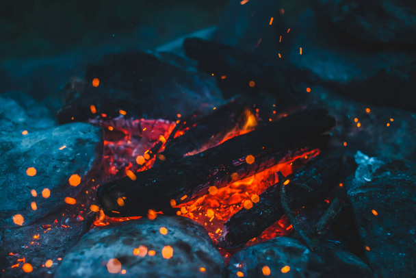 Vivid smoldered firewoods burned in fire closeup. Atmospheric background with orange flame of campfire. Wonderful full frame image of bonfire with glowing embers in air. Warm logs, bright sparks bokeh - Foto, Imagen