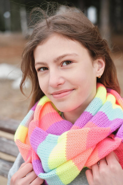tiener meisje draagt feestelijke gestreepte sjaal. outdoor portret van een gelukkige tiener op zoek naar een kijker. - Foto, afbeelding