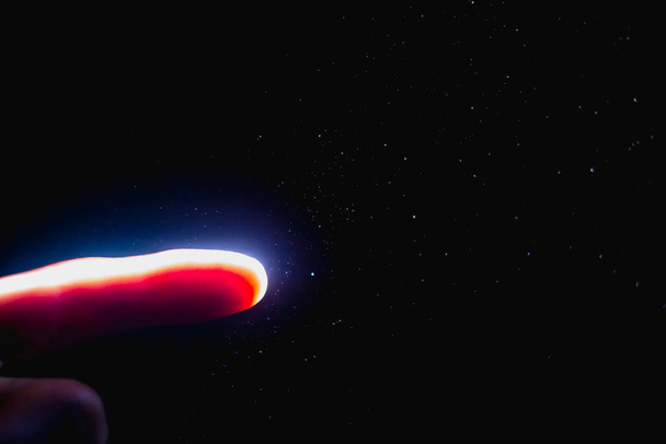 The finger is illuminated by a bright beam of light in the dark with flying dust particles. - Fotoğraf, Görsel
