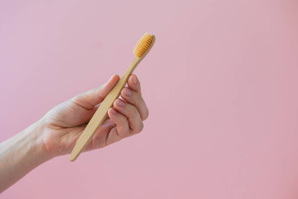 daily human hygiene, cotton swabs and cotton pads, a womans hand holding bamboo toothbrushes on a pink background in a glass or against a background of plants - Photo, Image