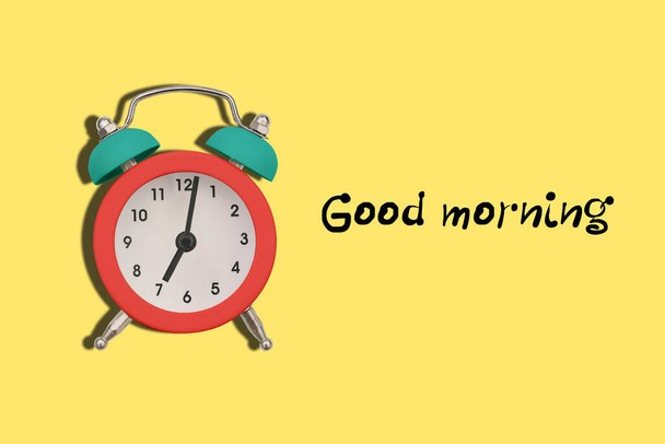生地と黄色の背景にカラフルな目覚まし時計おはようございます。時計は午前中に７時を示している。仕事に行く時間だ - 写真・画像