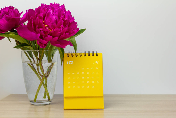 Kalender für Juli 2021 und Pfingstrosen auf dem Tisch. Desktop-Kalender für Planung, Terminplanung, Zuordnung, Organisation und Verwaltung jedes Datums - Foto, Bild