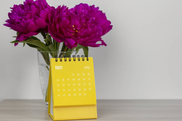 Kalender für Juli 2021 und Pfingstrosen auf dem Tisch. Desktop-Kalender für Planung, Terminplanung, Zuordnung, Organisation und Verwaltung jedes Datums. - Foto, Bild