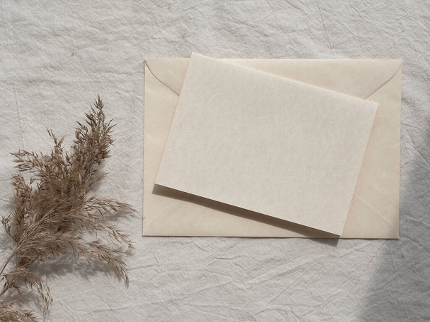 Minumal mockup, off white card and pampas grass. Simple minimal flat lay on ivory textile with dry brown earth colored reeds. Natural brown neutral beige flat lay. Direct natural light, shadows - Zdjęcie, obraz