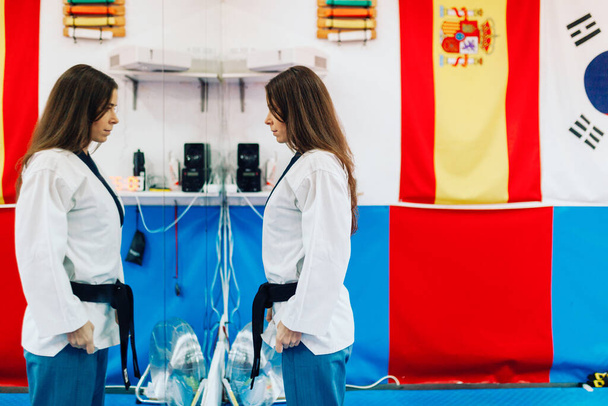 Young woman dresses in her taekwondo suit in front the mirror - Photo, Image