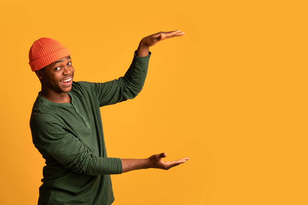 Positive Black Guy Holding Big Invisible Object In Hands Over Yellow Background - Φωτογραφία, εικόνα