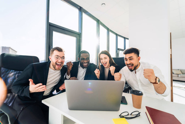 Az üzleti partnerek egy laptop előtt ülnek az irodában, és örülnek a győzelemnek. - Fotó, kép