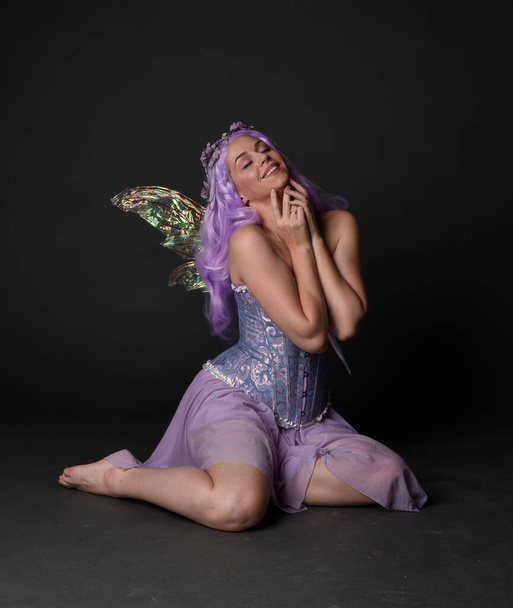 Pełna długość portret fioletowy włosy dziewczyna noszenie gorset fantasy sukienka z bajki skrzydła i korony kwiatowej. Posadzona na ciemnym tle studia. - Zdjęcie, obraz