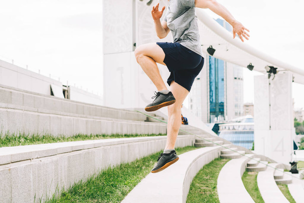 Νεαρός αθλητής δρομέας τρέχει πάνω-κάτω στις σκάλες της πόλης το καλοκαίρι για πρωινό τρέξιμο, φόντο αστικού δρόμου της πόλης. Αθλητική προπόνηση. Γυμναστική άσκηση καρδιο στον καθαρό αέρα, άλμα έξω - Φωτογραφία, εικόνα