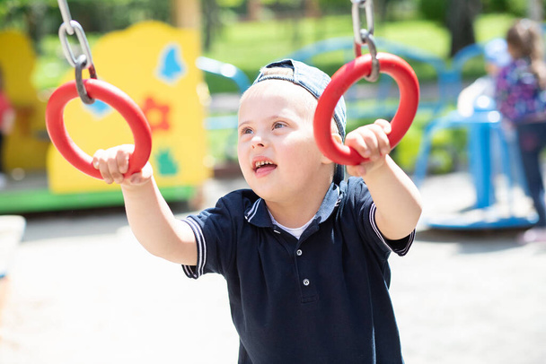 Chłopiec z zespołem Downa bawi się na placu zabaw, dziecko niepełnosprawne, dziecko z dodatkowym chromosomem. - Zdjęcie, obraz