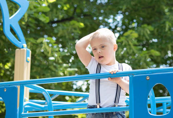 Ein Junge mit Down-Syndrom spielt auf dem Spielplatz, ein behindertes Kind, ein Kind mit einem zusätzlichen Chromosom. - Foto, Bild