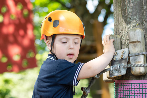 Un ragazzo felice con la sindrome di Down in un casco arancione passa attraverso un compito sportivo difficile, un bambino disabile, intrattenimento sportivo per bambini. - Foto, immagini