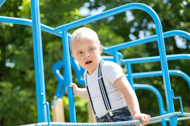Egy Down-szindrómás fiú játszik a játszótéren, egy fogyatékos gyerek, egy extra kromoszómás gyerek.. - Fotó, kép