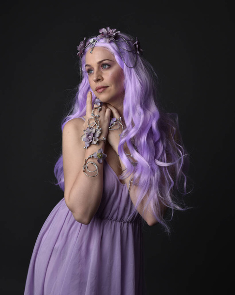 Lähikuva muotokuva violetti tukka tyttö yllään fantasia korsetti mekko keiju siivet ja kukka kruunu, valu loitsu. Poseeraus tummaa studiotaustaa vasten. - Valokuva, kuva