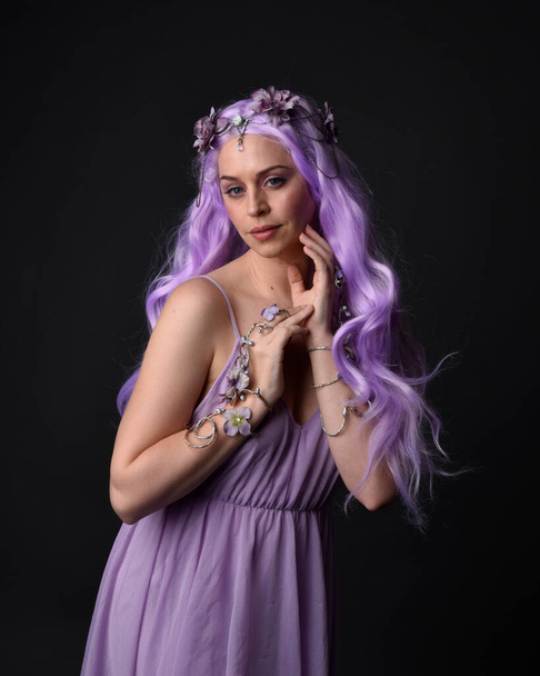 Zblízka portrét fialové vlasy dívka na sobě fantasy korzet šaty s víla křídla a květinové koruny, seslal kouzlo. Posing against a dark studio background. - Fotografie, Obrázek