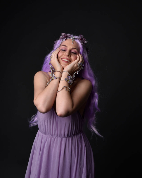 Close up portrait of a purple haired  girl wearing fantasy corset dress with fairy wings and flower crown, casting a spell.  Posing against a dark studio background. - Fotó, kép