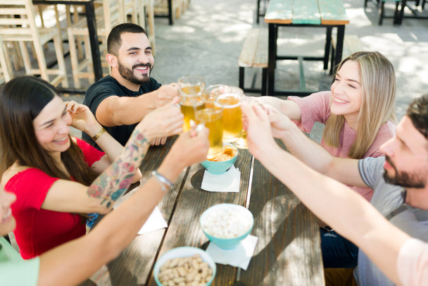 Díky! Veselá skupinka přátel pronáší přípitek s pivem. Nejlepší přátelé si spolu užívají pár drinků ve venkovním baru a oslavují - Fotografie, Obrázek