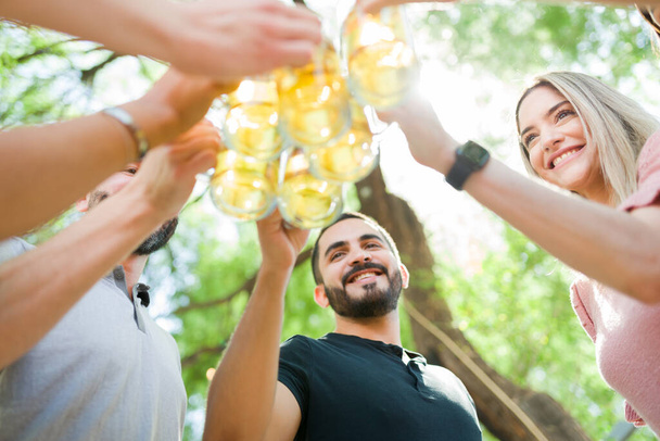 Ευτυχισμένοι φίλοι κάνουν πρόποση με μπύρα. Νεαρές γυναίκες και άνδρες γιορτάζουν μαζί και απολαμβάνουν μερικά ποτά σε ένα μπαρ - Φωτογραφία, εικόνα