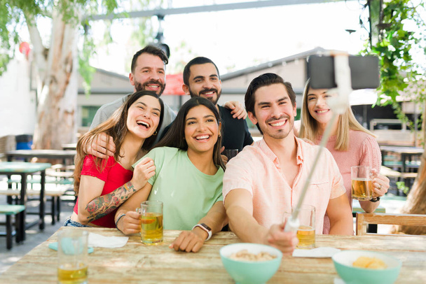 Hauska monirotuinen ryhmä ystäviä hymyilee selfielle istuessaan yhdessä baarissa. Sulje college ystävät ottavat kuvan älypuhelimella lähettää sosiaalisen median - Valokuva, kuva