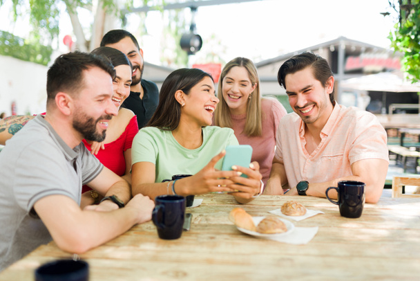 Betrachten wir Online-Inhalte. Diverse Freunde lachen und achten auf ein lustiges Bild oder Video auf dem Smartphone, während sie in einem Café abhängen  - Foto, Bild