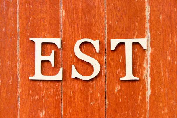 Písmeno abecedy ve slově EST (zkratka zavedeného, odhadovaného, východního časového pásma, značeno posloupností) na starém červeném pozadí barevného dřeva - Fotografie, Obrázek