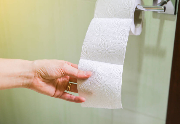 Μια γυναίκα κρατάει χαρτί τουαλέτας στο χέρι της.. - Φωτογραφία, εικόνα