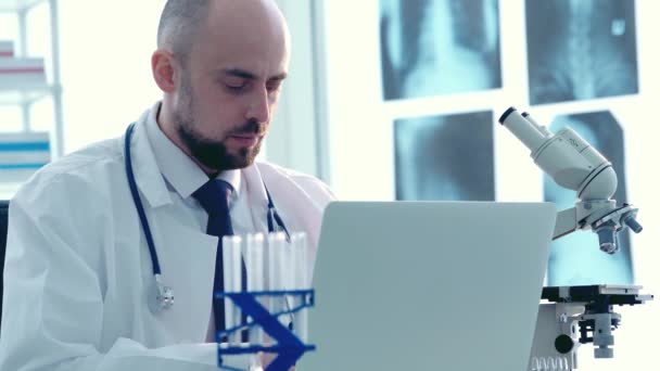 medical researcher, looking in the microscope while doing some analysis and typing them in the laptop computer at the laboratory. - Materiał filmowy, wideo