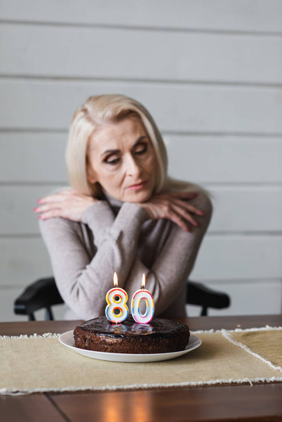 Birthday cake with candles in shape of eighty numbers on table near blurred senior woman  - Fotoğraf, Görsel