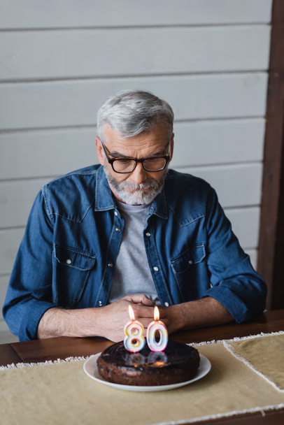 Senior man looking at blurred birthday cake on table  - Φωτογραφία, εικόνα