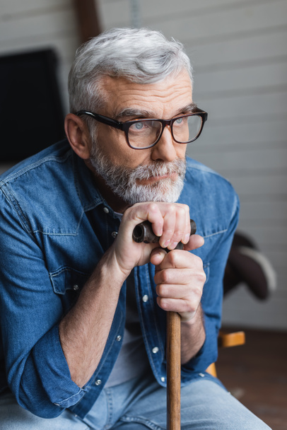 Elderly man in eyeglasses holding crutch at home  - Photo, image