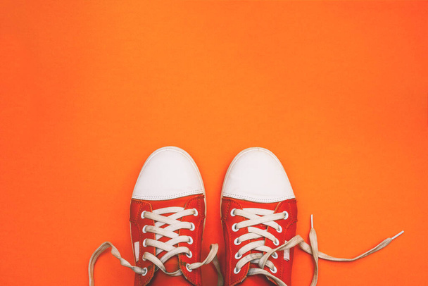 Red sneakers with untied laces with copy space. Youth sneakers on an orange background. Top view, flat lay - Photo, Image