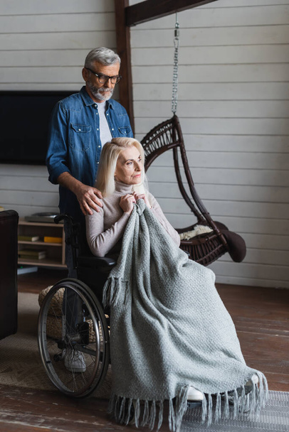 Elderly man embracing wife in wheelchair with blanket - Photo, Image