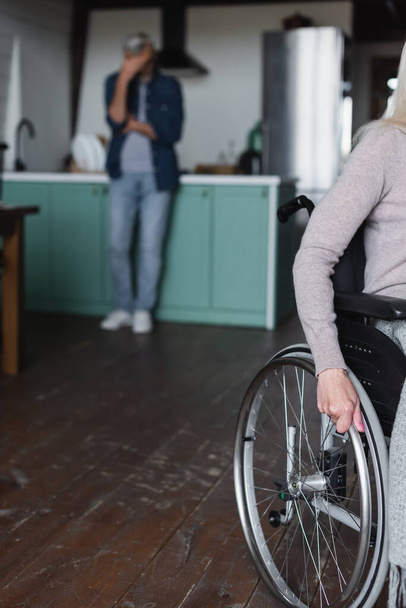 Kobieta na wózku inwalidzkim w pobliżu zamazanego męża w kuchni  - Zdjęcie, obraz