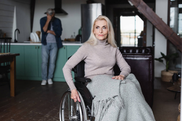 Senior woman in wheelchair near husband on blurred background  - Fotoğraf, Görsel