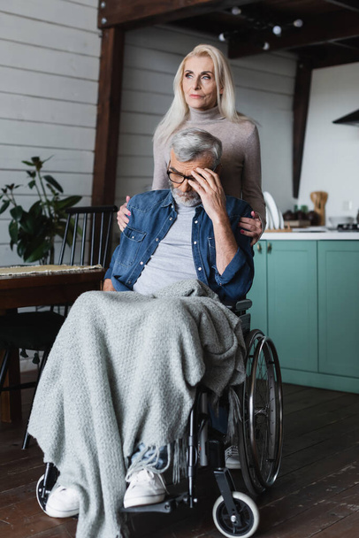 Voorzichtige vrouw omhelst trieste man in rolstoel thuis  - Foto, afbeelding