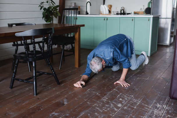 Uomo anziano con stampella che cade sul pavimento in cucina  - Foto, immagini