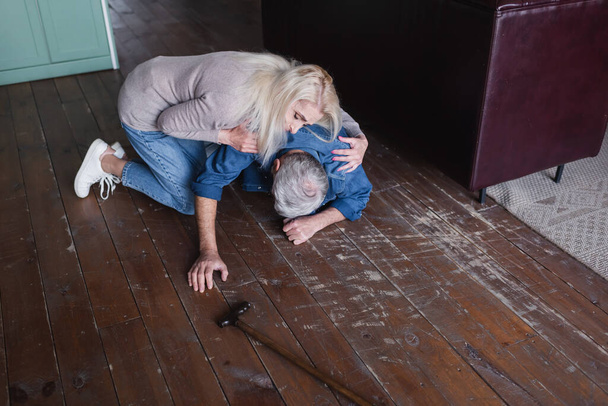 Elderly woman hugging sick husband near crutch on floor  - Fotoğraf, Görsel