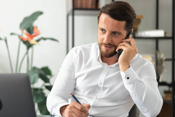 Successful Caucasian business man talking on mobile phone while sitting in the office, discussing a deal, manager, talks on a smartphone with colleagues - 写真・画像