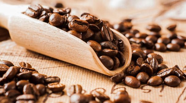 Closeup of coffee beans background.coffee beans on wooden table. Background of ground coffee texture. Coffee beans are scattered on the table. - Photo, image