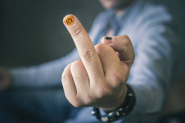 Środkowy palec pokazywany jest przez mężczyznę w niebieskiej koszuli. FCK jest napisane na żółtym gwoździu, projekt męskiego manicure. Nieprzyzwoity gest przed kamerą. Negatywne emocje. biznesmen nieszczęśliwy - Zdjęcie, obraz