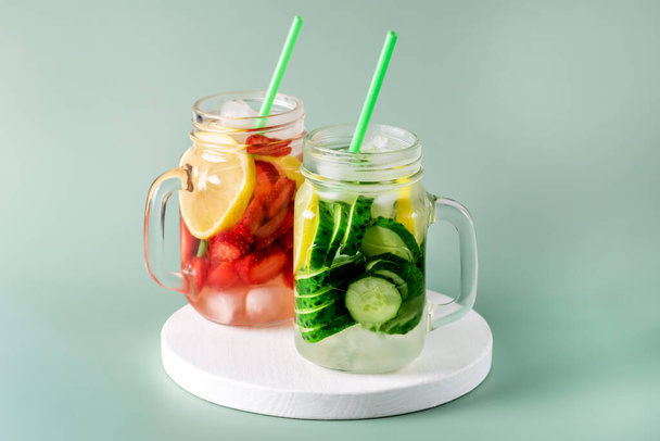 Разнообразие холодных летних напитков в стеклянных банках, наполненных детоксикационной водой с огуречным лимоном и клубникой Здоровый напиток зеленый фон - Фото, изображение