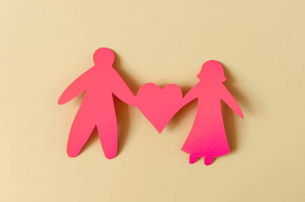 Bright red figures of two people holding a heart on a colored background. The concept of a happy relationship. Cardboard figures of people - Foto, Imagem