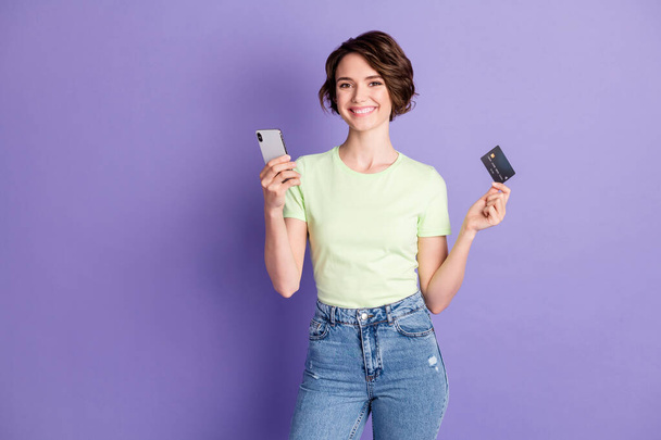 Retrato de chica alegre agradable sosteniendo en las manos tarjeta bancaria utilizando tienda de dispositivos de pago comprar web navegar aislado sobre fondo de color violeta - Foto, Imagen