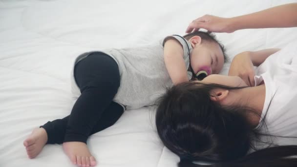 Mladá asijská matka dotek hlava malé holčičky s něhou na posteli v ložnici, maminka milují novorozence a péči, žena s výrazem s dítětem spolu, rodič a dcera, rodinný koncept. - Záběry, video