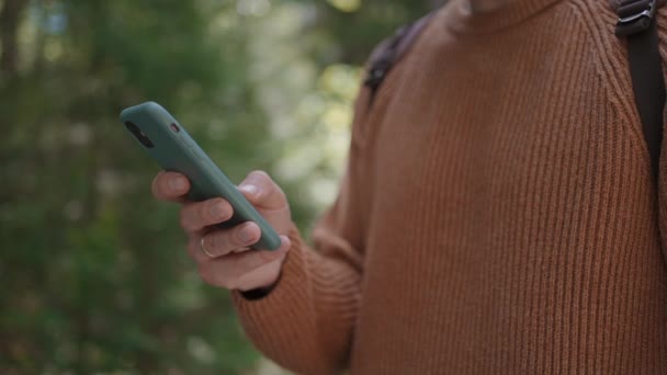 Primer plano de un teléfono móvil en manos de un viajero masculino caminando por el bosque. Redes sociales Navegador y mensajero. Utilice su teléfono móvil para dar un paseo por el bosque - Metraje, vídeo