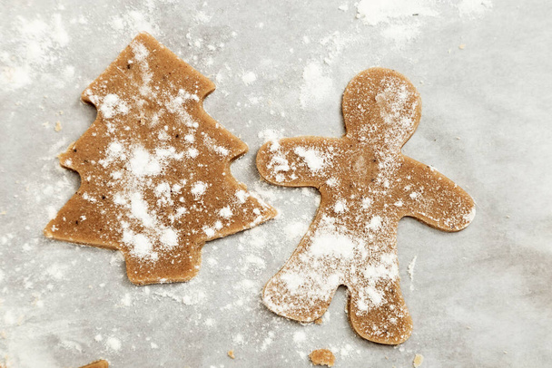 Gingerbread Cookie. New Year figures from a dough, prepared for baking in the oven. Raw cookies in the form of Christmas tree and gingerbread man on paper for baking. Christmas food concept. - Zdjęcie, obraz