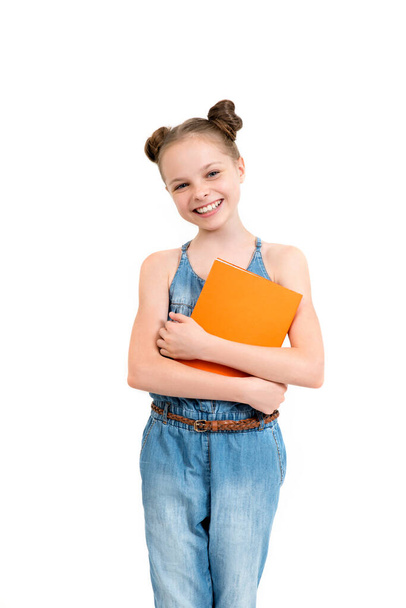 Happy cute smiling child girl in denim overalls holding books.  Schoolgirl with facial expression isolated on white. Concept of education, reading, back to school. - Zdjęcie, obraz